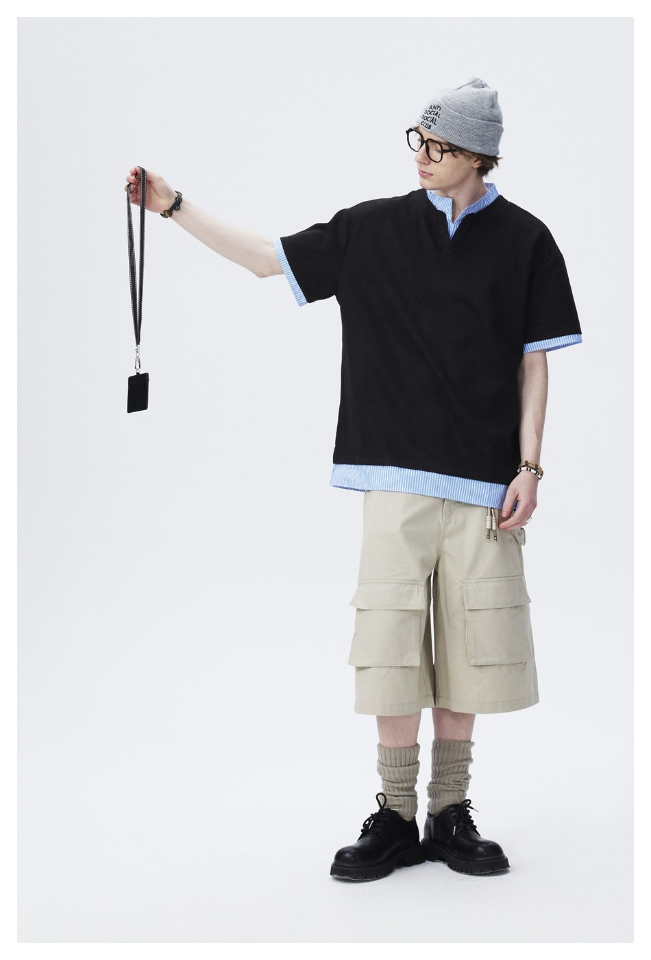 Model wearing an oversized black V-neck short-sleeve tee over a blue-and-white striped shirt, with beige cargo shorts.