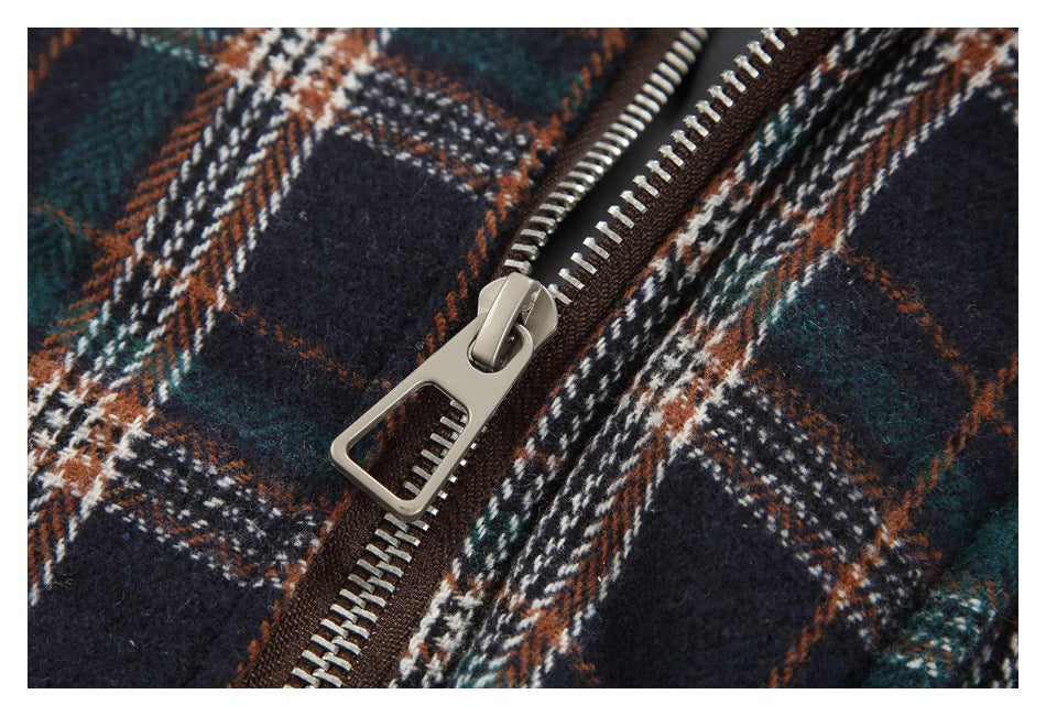 Close-up of a silver zipper and large pull against dark navy, green, rust, and white plaid fabric.