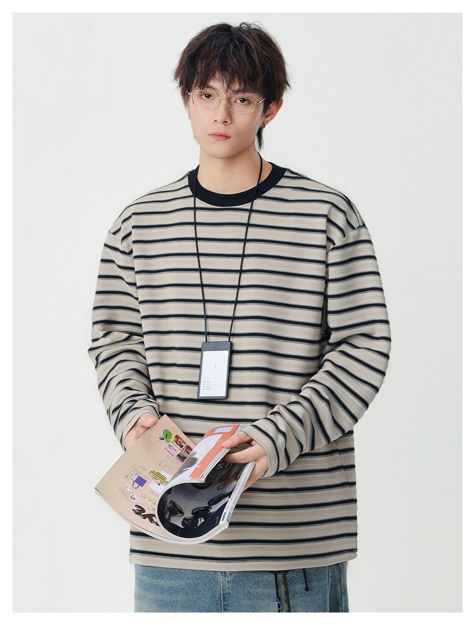 Model wearing khaki striped long-sleeve top with black collar while holding a magazine, with jeans