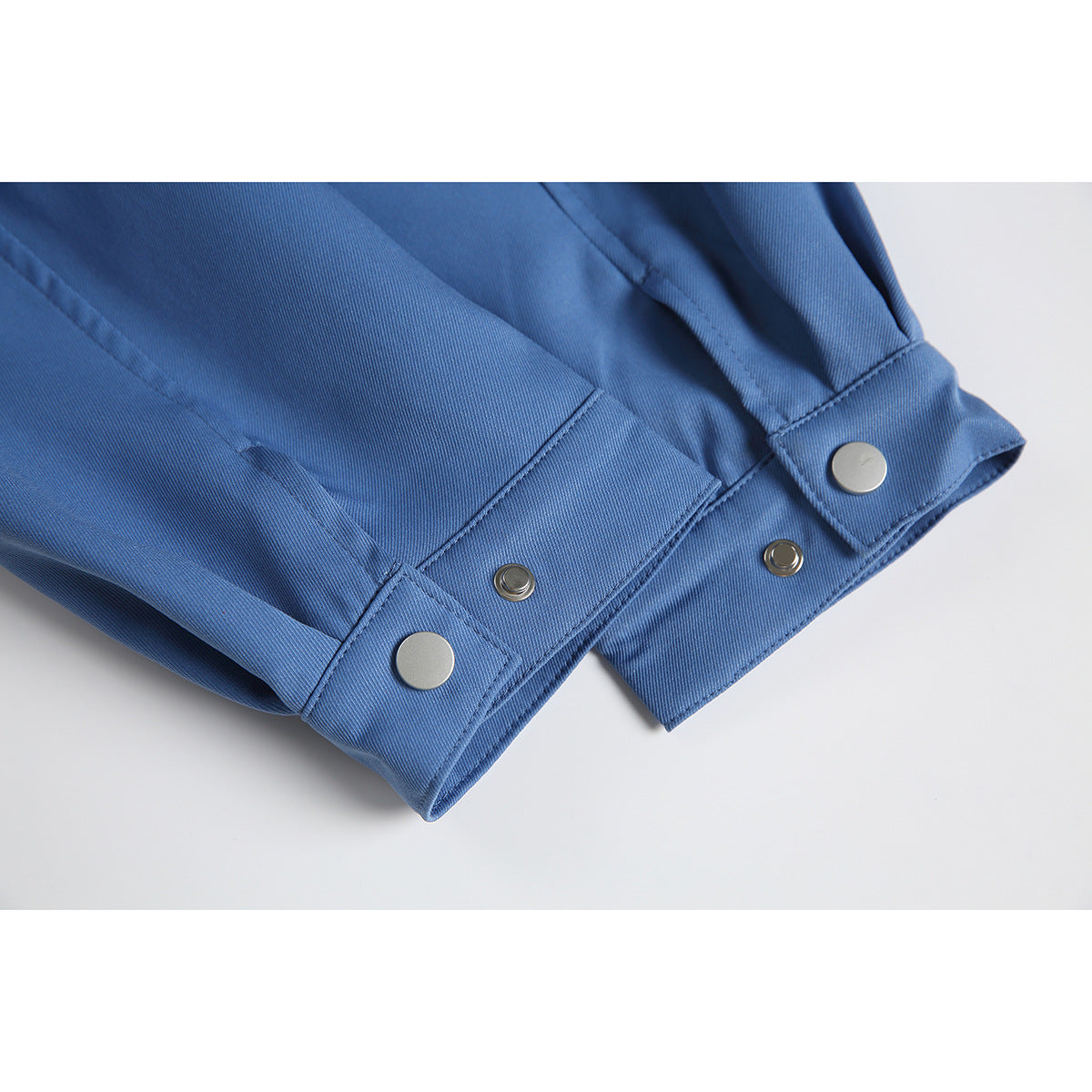 Close-up of blue jacket sleeve cuffs with adjustable tabs and metal snap fasteners.