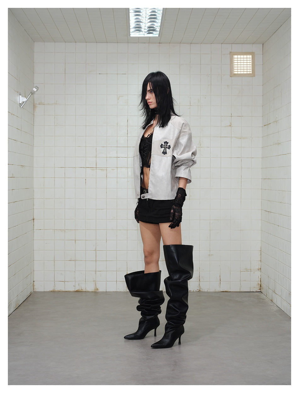 Model wearing a light gray cropped jacket with a black cross appliqué, black shorts, lace gloves, and tall black boots.