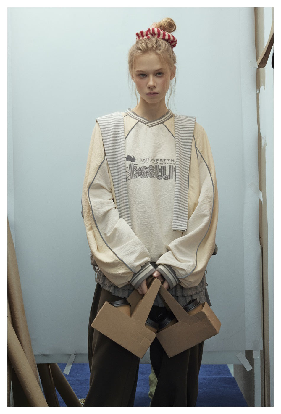 Front view of a model in a cream sweatshirt with a chest graphic, striped neckline and cuffs, and contrast piping.
