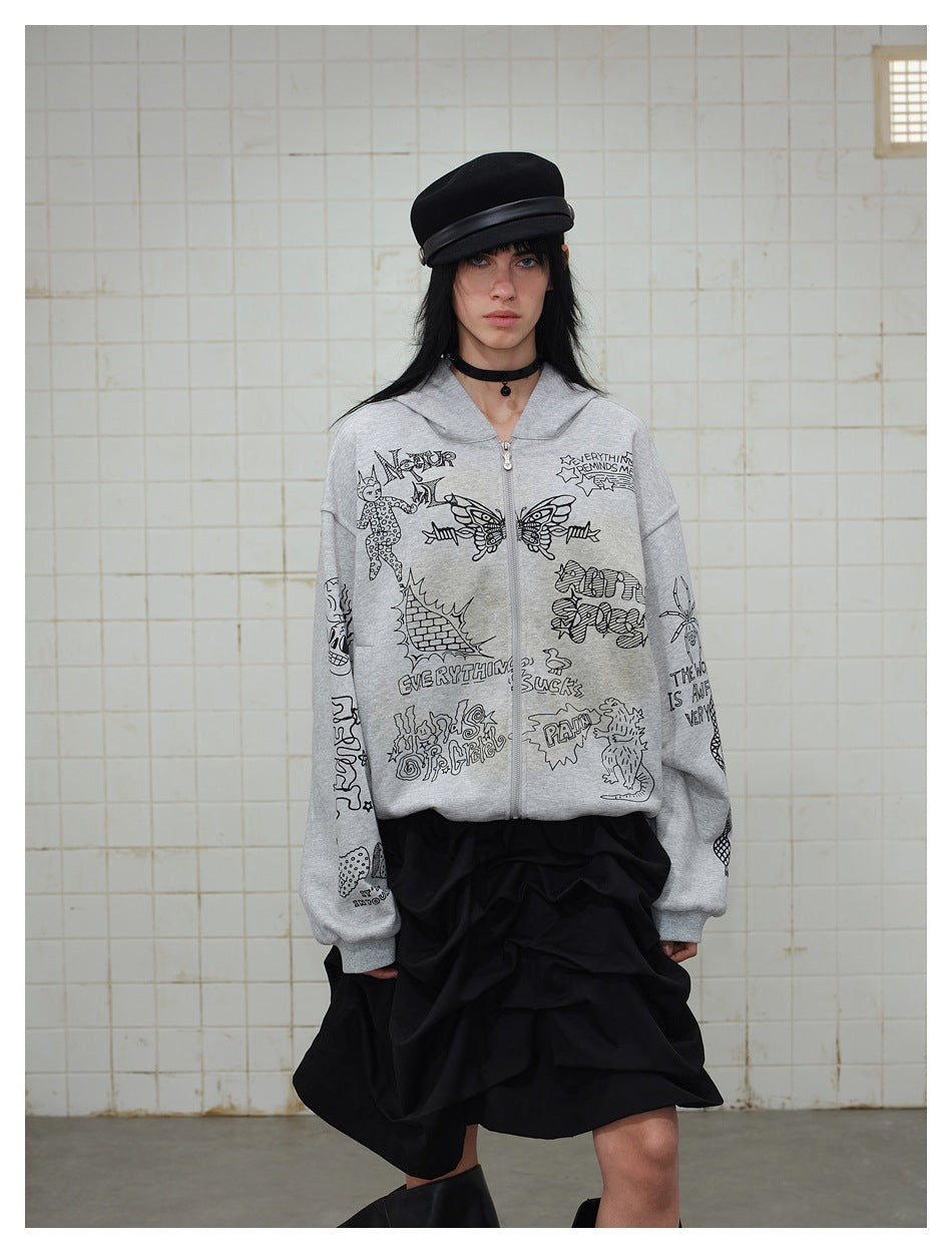 Model wearing a gray illustrated zip-up hoodie with a black ruffled skirt and black cap.