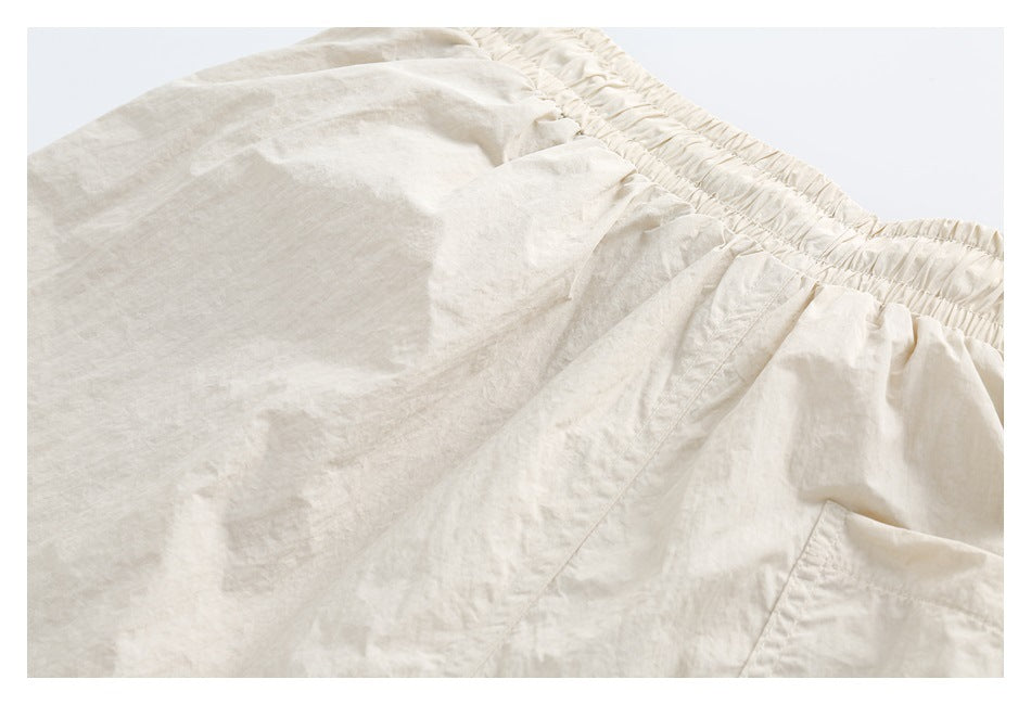 Close-up of light cream bottoms with a gathered elastic waistband and part of a side pocket.