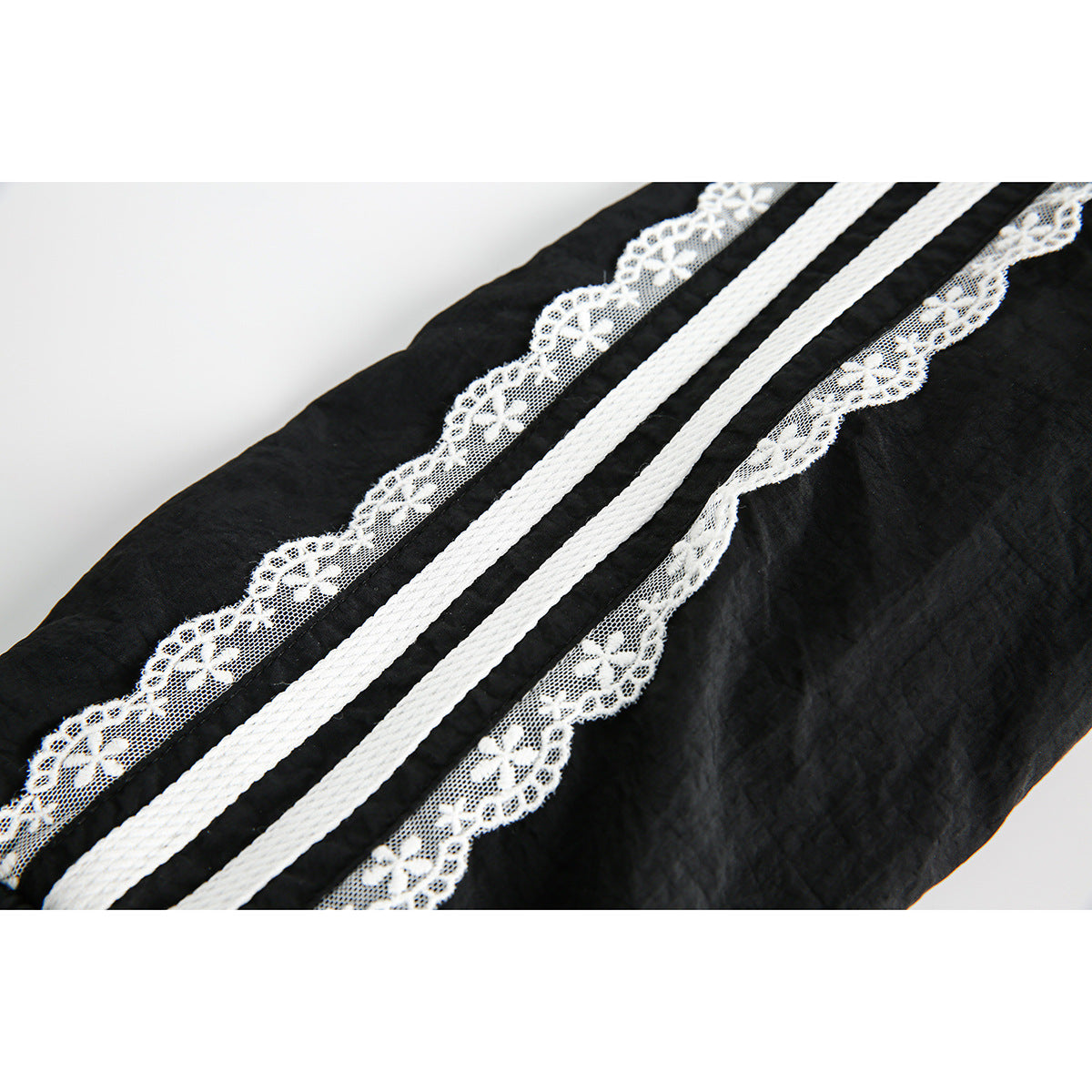 Close-up of white braided stripes and scalloped floral lace trim running along the black jacket sleeve.