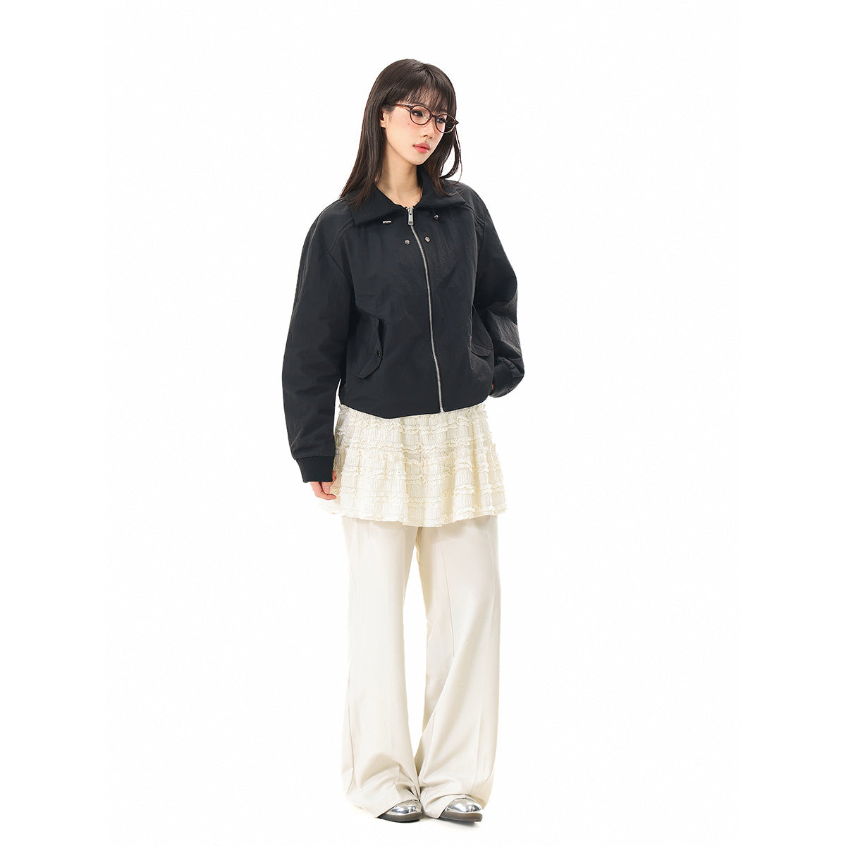 Model wearing a black zip-front jacket with a wide collar and flap pockets, styled with a cream lace skirt and trousers.