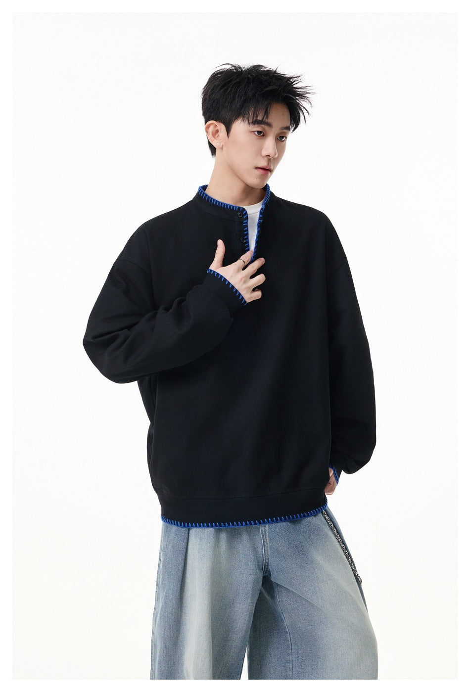 Model wearing a black oversized pullover with blue contrast stitching at the collar, cuffs and hem.