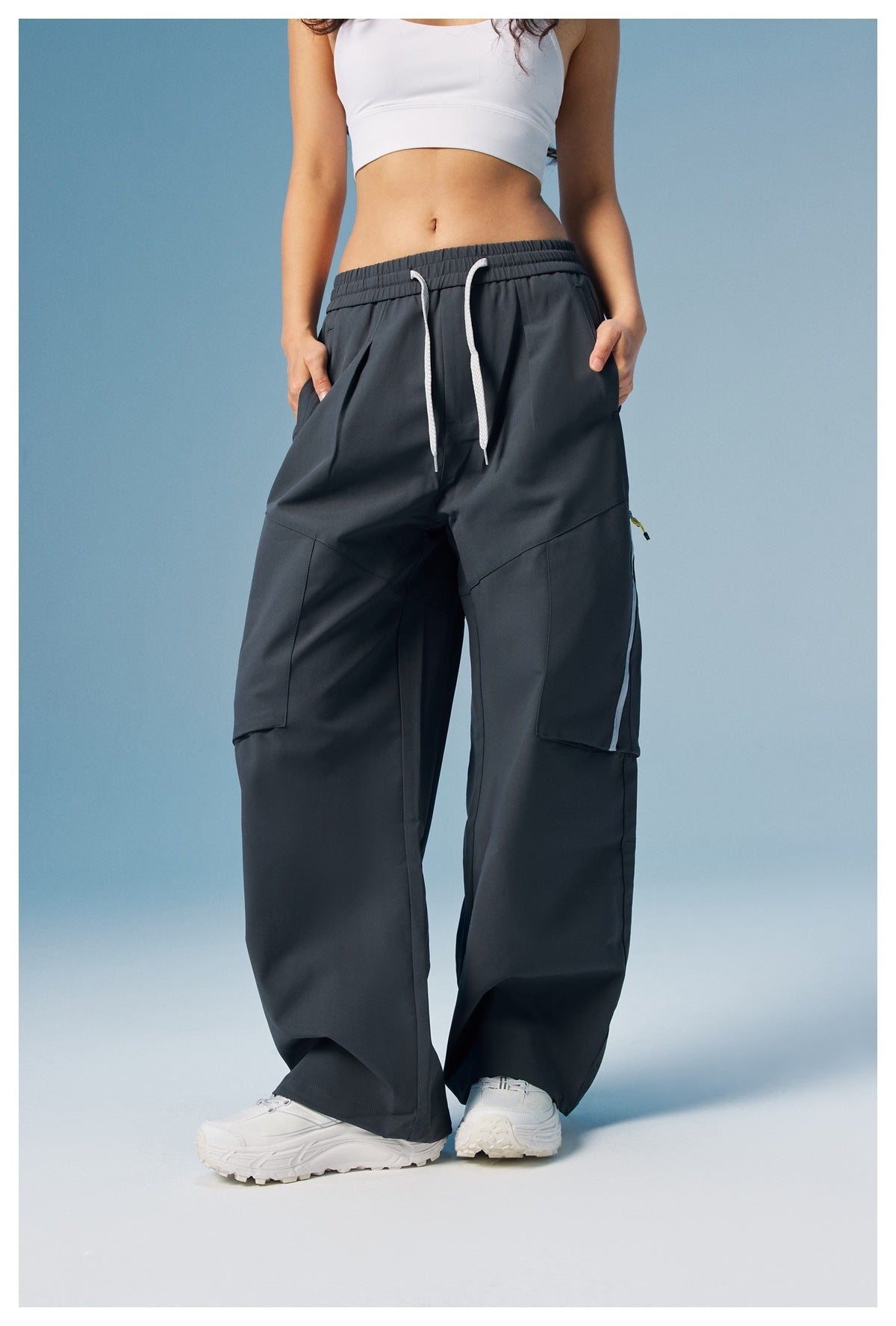 Front view of a model wearing charcoal wide-leg cargo pants with white drawstrings and large side pockets.