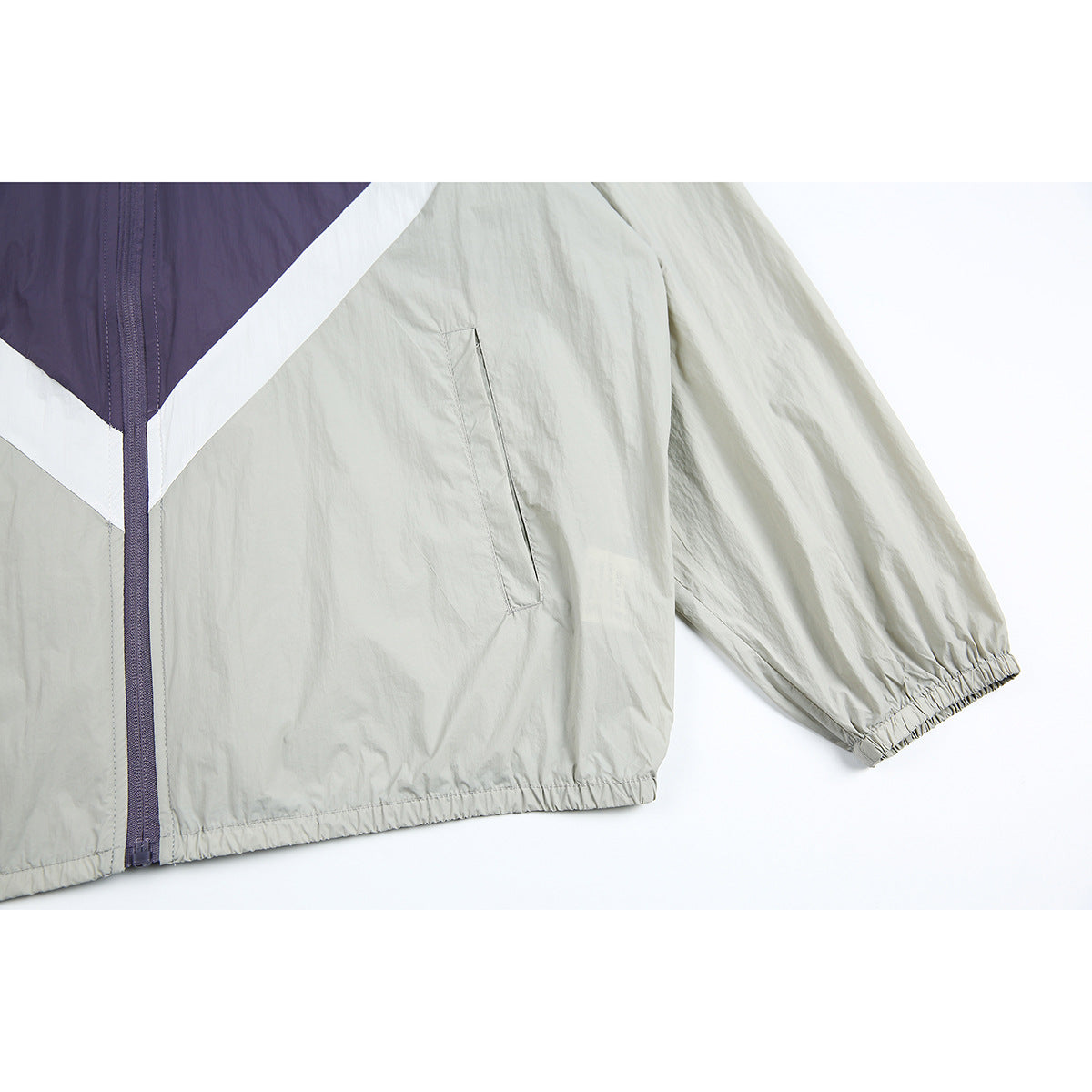 Close-up of a light gray jacket sleeve, elastic cuff and hem, front zipper, and slanted pocket.