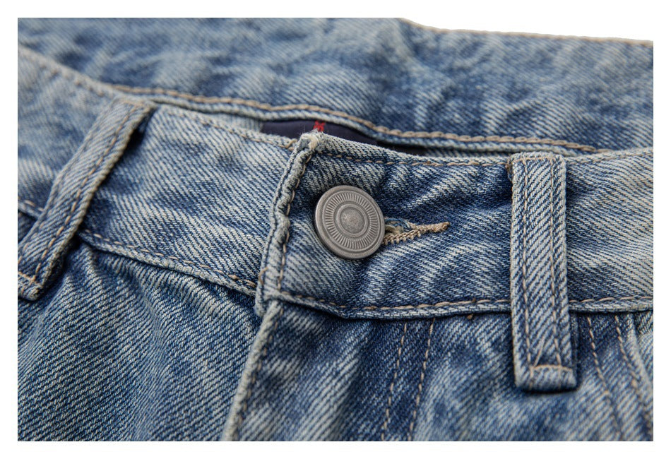 Close-up of light-wash blue jeans showing the metal waist button, belt loop, and contrast stitching.