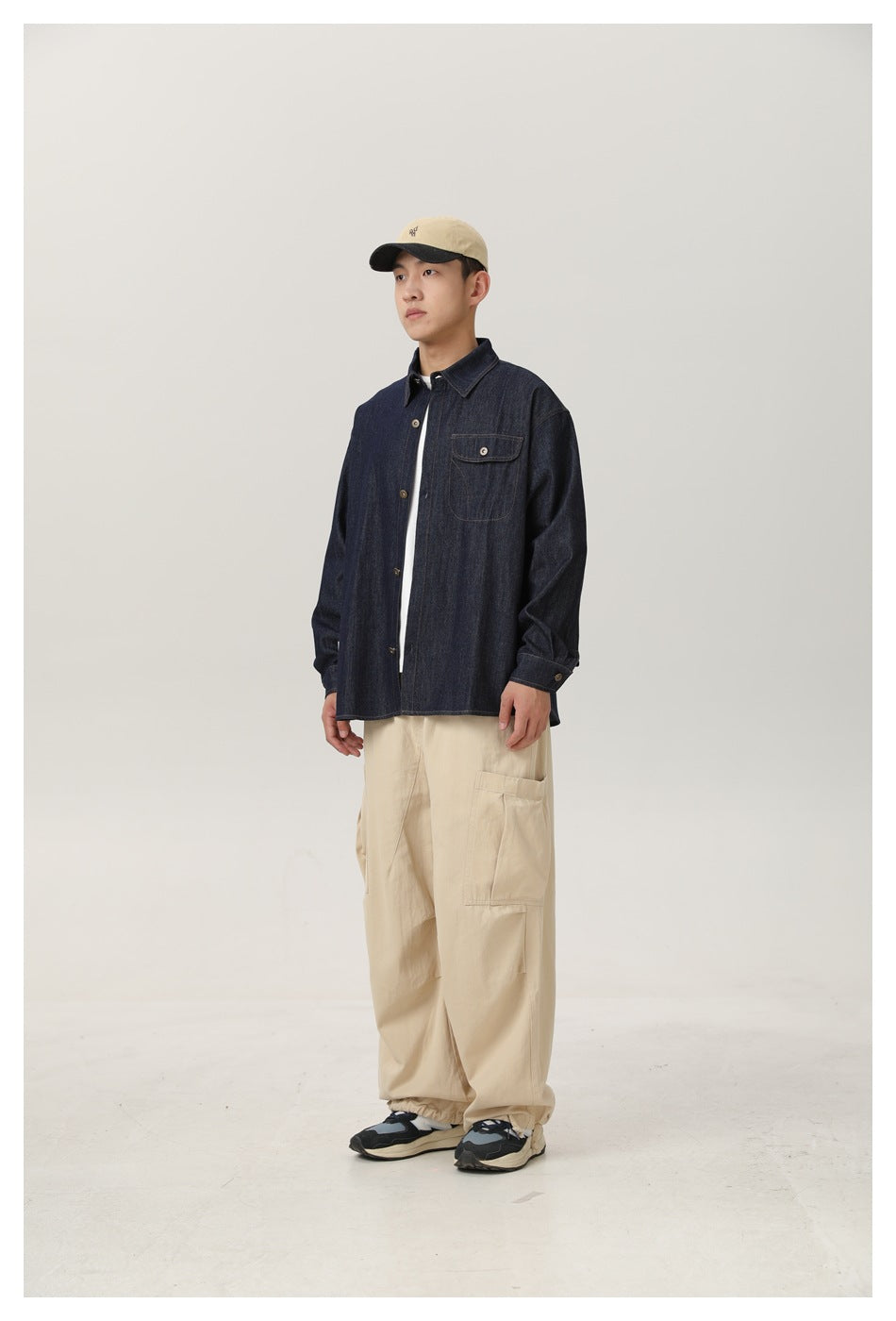 Model wearing an open dark denim shirt over a white tee with beige cargo pants and a cap, side view
