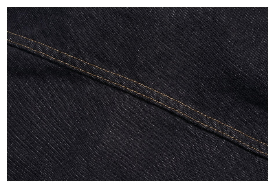 Close-up of dark denim fabric and a diagonal seam with tan contrast stitching.