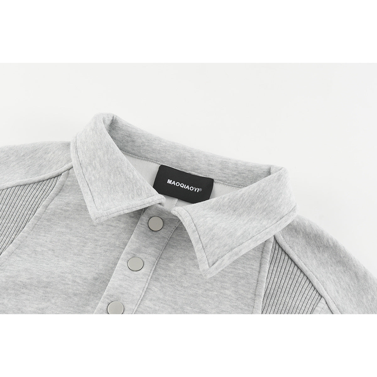Close-up of a light gray collared sweatshirt with silver snap buttons and ribbed shoulder panels.