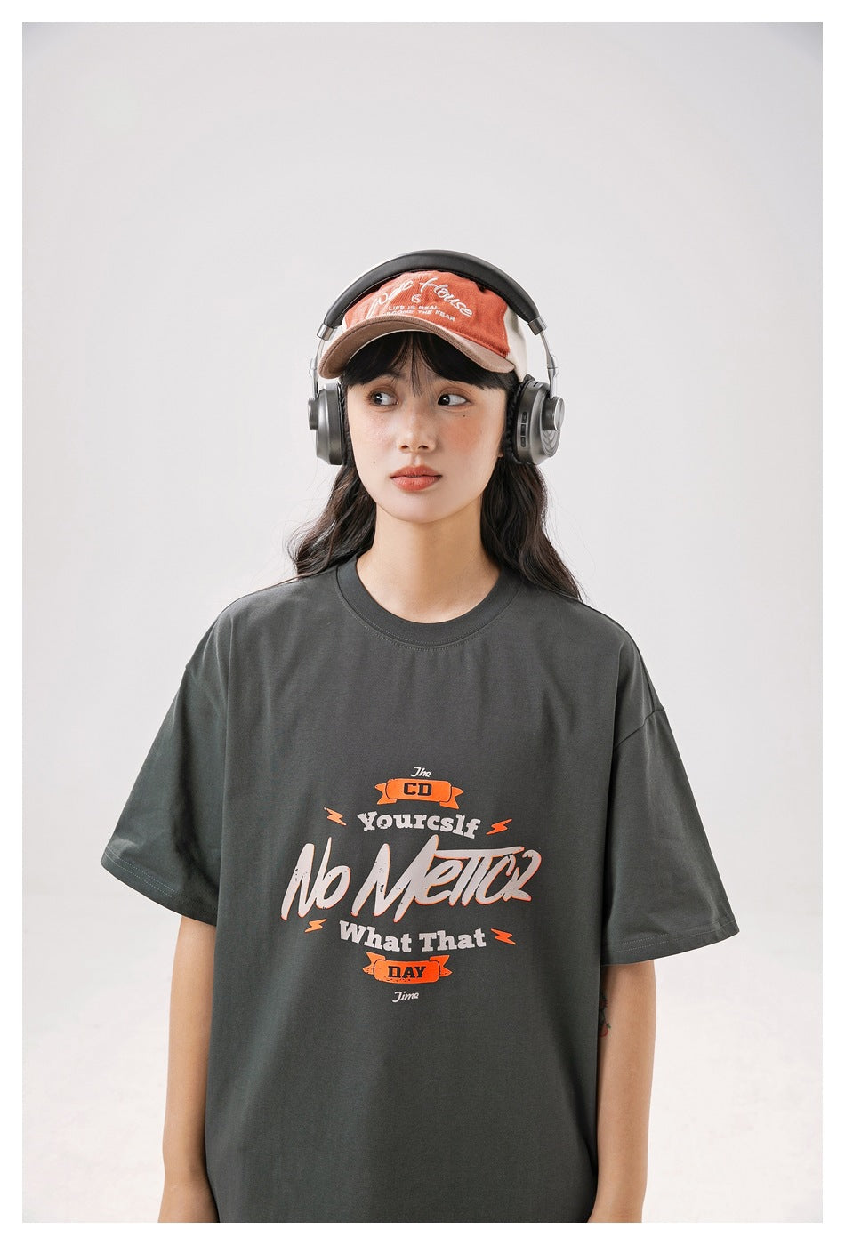 Model wearing a charcoal oversized T-shirt with a large cream and orange graphic across the front.