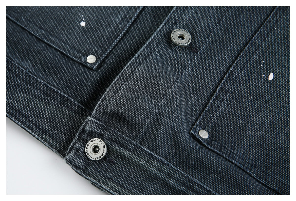 Close-up of dark textured denim panels with several silver snaps and small white paint flecks.