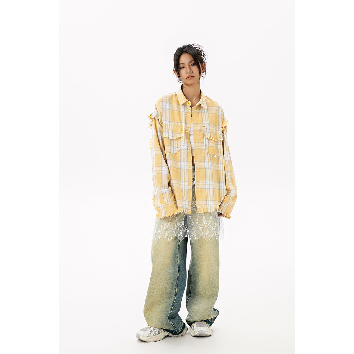 Full-length view of a model in an oversized yellow plaid shirt with frayed details, lace overlay, wide-leg jeans, and