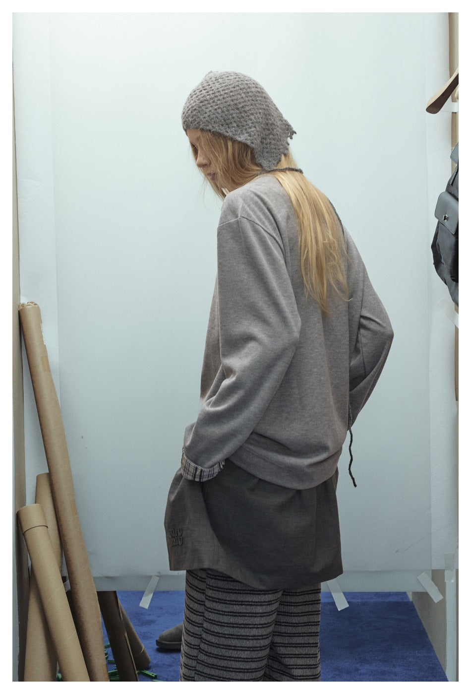 Three-quarter back view of a model in a loose gray top with plaid cuffs and dark shorts over striped trousers.