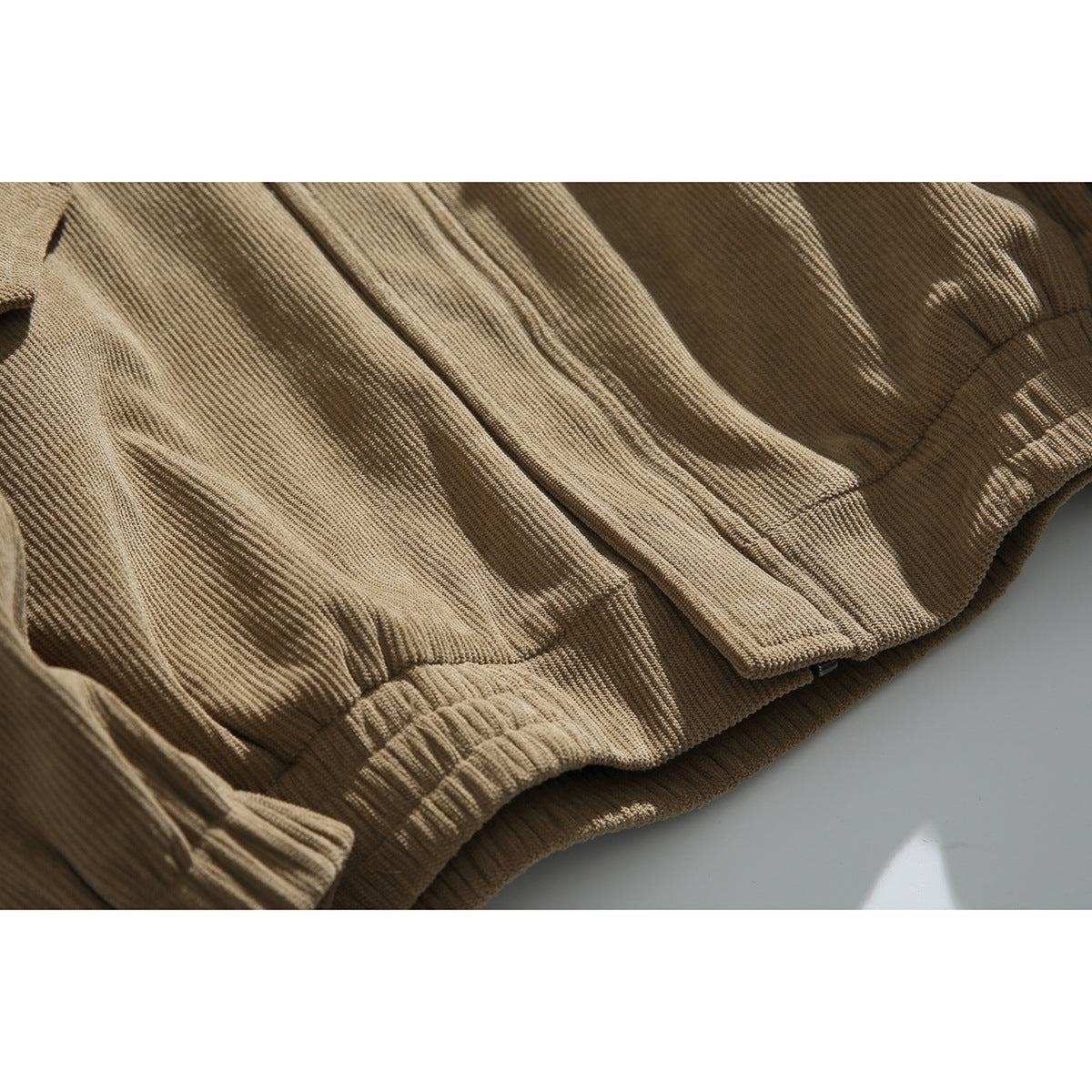 Close-up of a tan corduroy jacket's flap pocket, seams, and elastic hem.