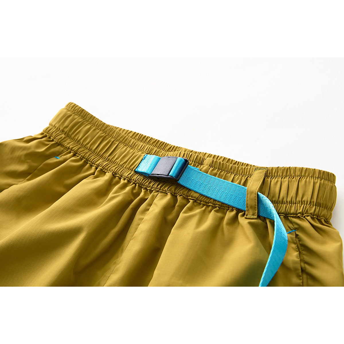 Close-up of mustard-yellow shorts with a gathered waistband, turquoise webbing belt and black buckle.