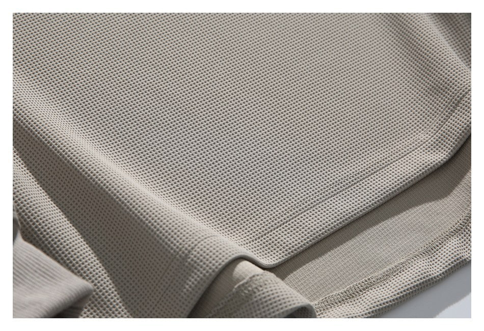 Close-up of taupe waffle-knit garment fabric with a stitched edge and folded hem.