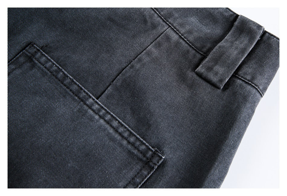 Close-up of dark charcoal denim trousers showing a belt loop and the edge of a stitched pocket.