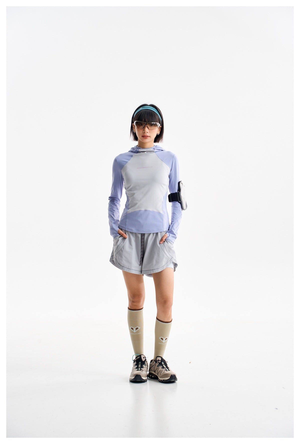 Model wearing a lavender and light gray hooded long-sleeve top with gray running shorts and knee-high socks.
