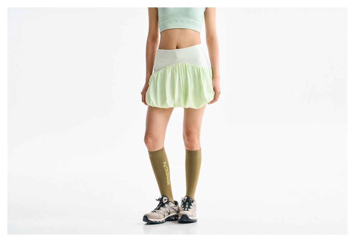 Back view of a model wearing a pale lime-green bubble skirt and olive knee-high socks.