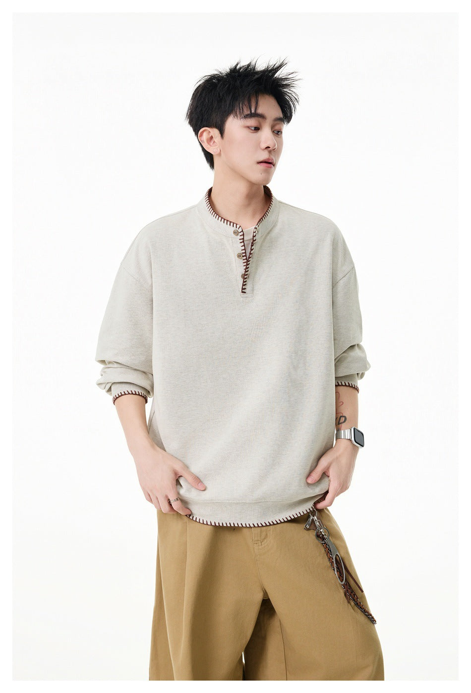 Model wearing a beige Henley sweatshirt with brown whipstitch trim, styled with khaki wide-leg pants