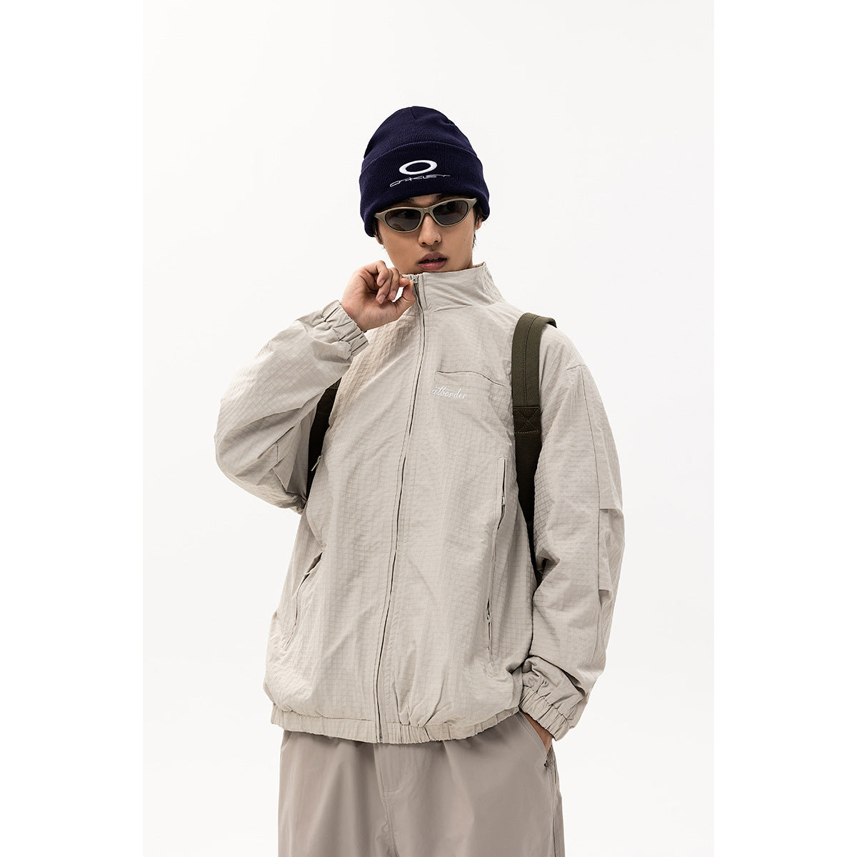 Model wearing a light gray zip-front jacket with a high collar and zip pockets, shown from the front.