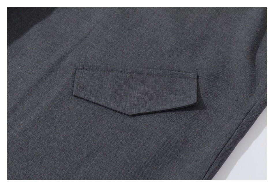 Close-up of a stitched, angular flap pocket on charcoal gray trousers.