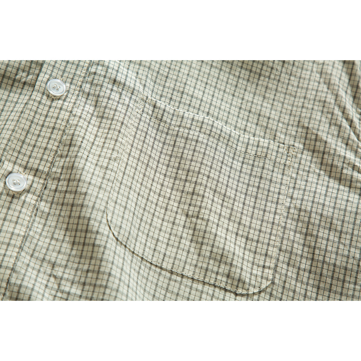 Close-up of the cream plaid shirt's chest pocket, stitching, and white buttons.