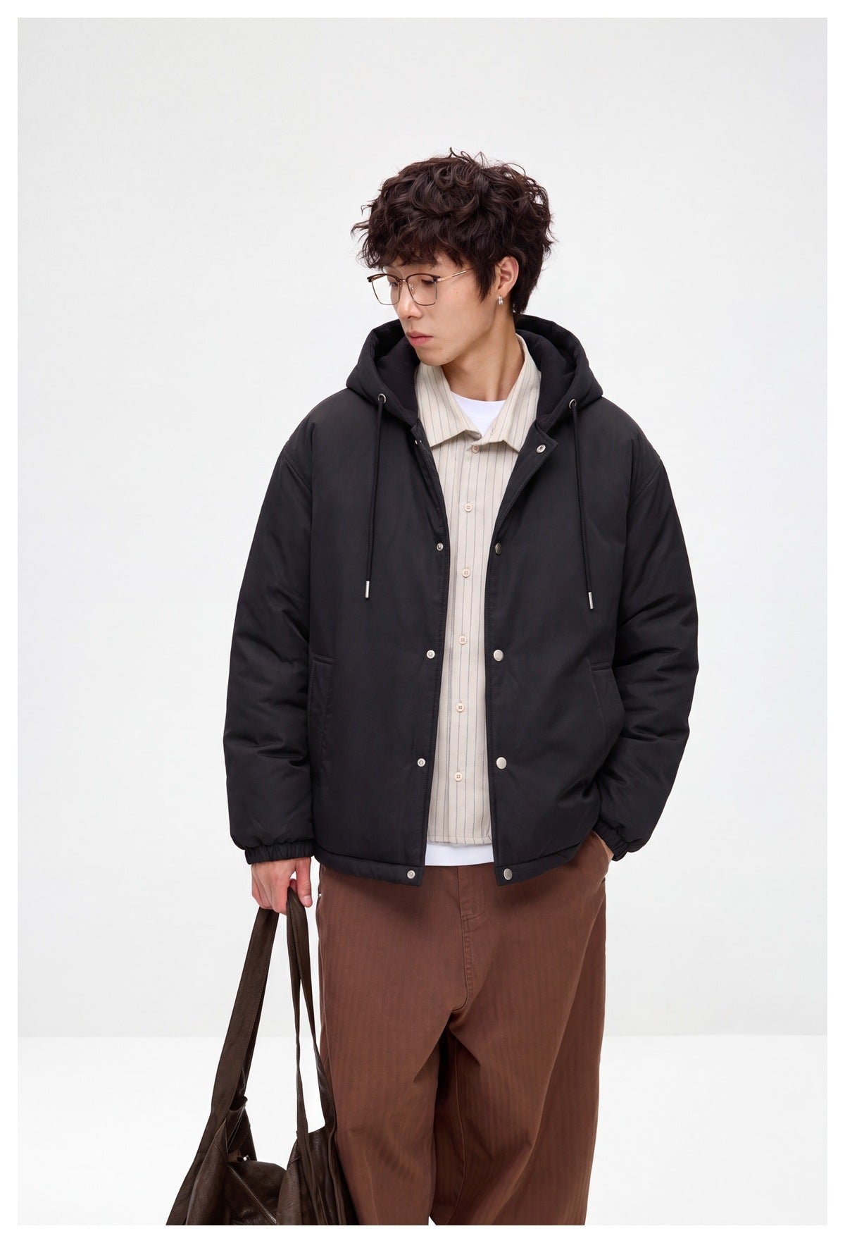 Model wearing a black hooded jacket with drawstrings, snap closure, and side pockets, shown from the front.