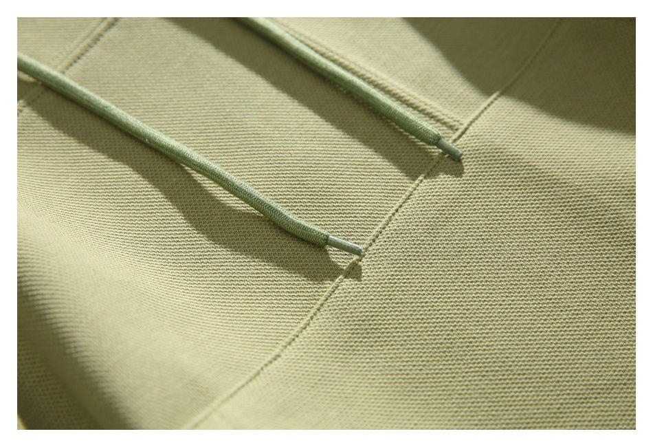 Close-up of the olive-green hoodie fabric, seam, and drawstring ends.
