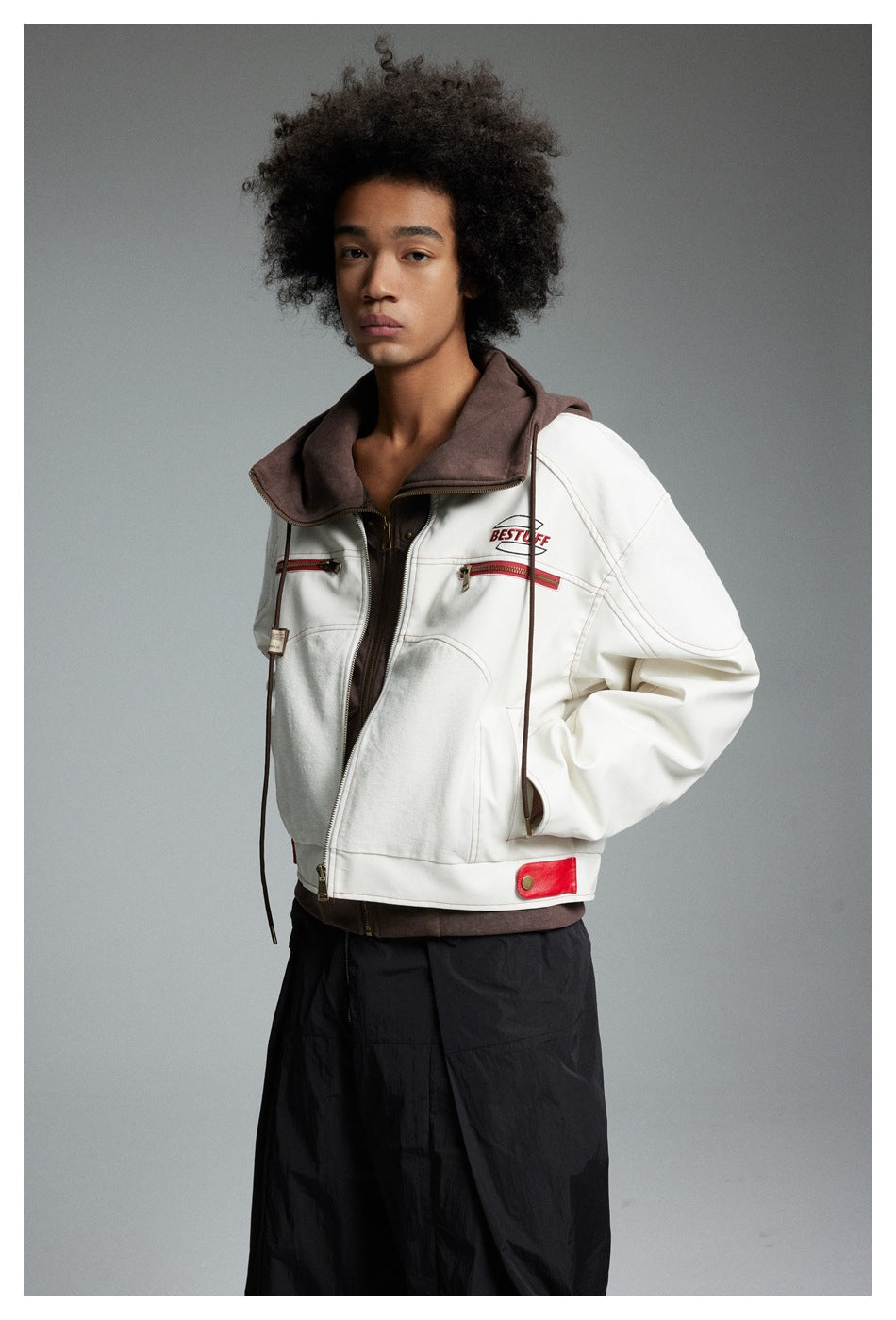 Model in a cream jacket with a wide brown hood, red zip pockets and accents, shown at a slight angle.
