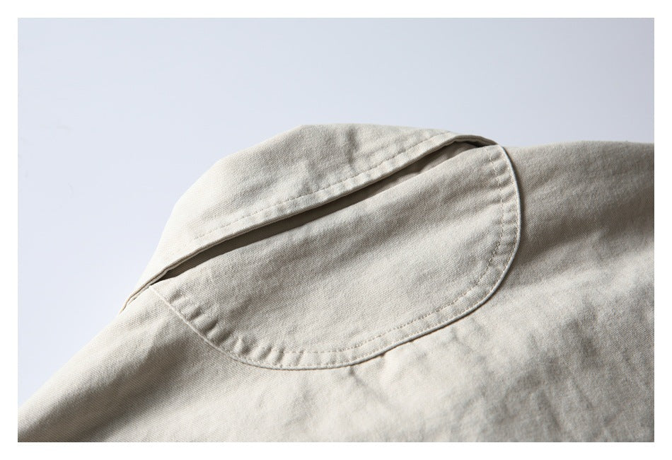 Close-up of the pointed collar and curved seam of a light beige jacket.
