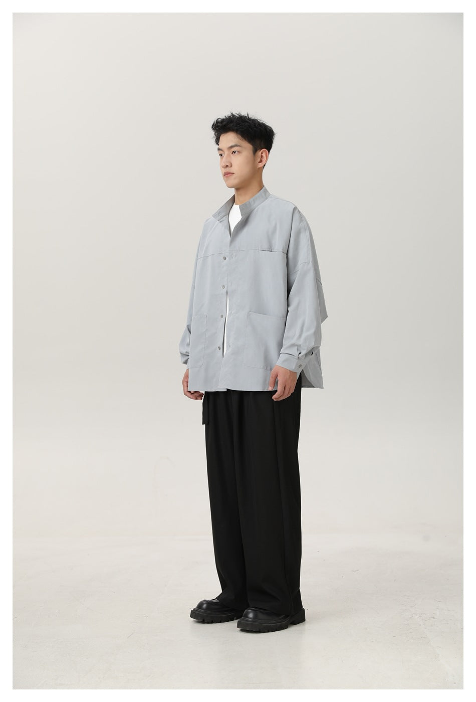 Model wearing a light gray oversized stand-collar shirt open over a white tee with black wide-leg pants