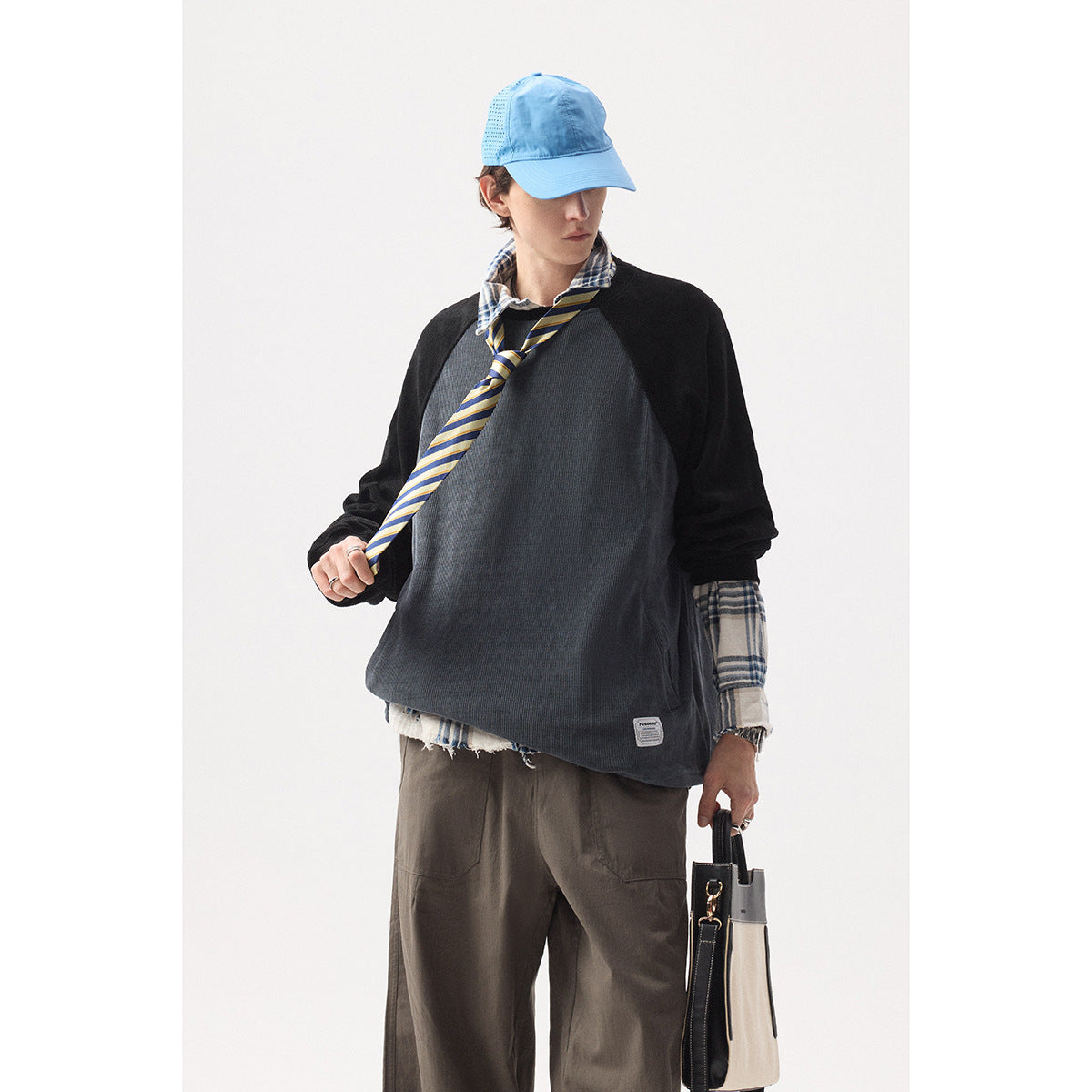 Closer view of a model wearing a charcoal pullover with black raglan sleeves over a plaid shirt and striped tie.