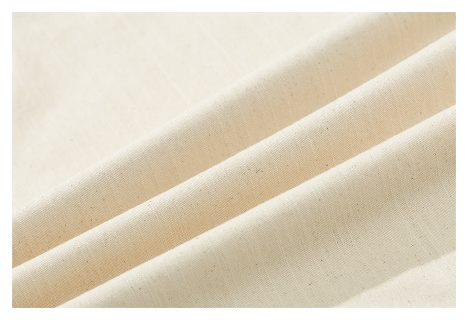 Close-up of cream-colored fabric folded into ridges, showing its woven texture and small flecks.