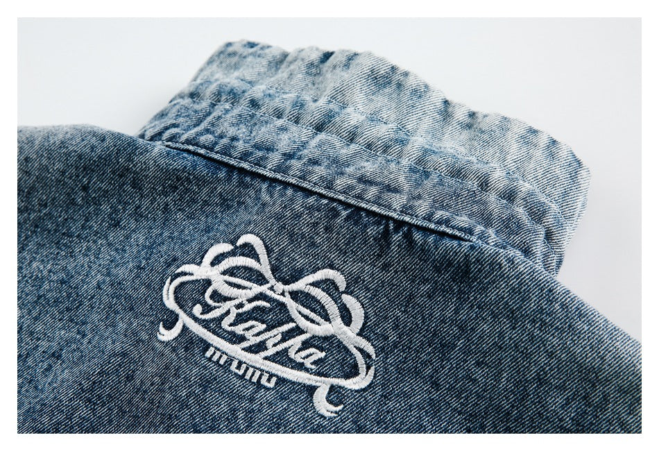 Close-up of blue denim with ornate white embroidery and visible stitched seams.