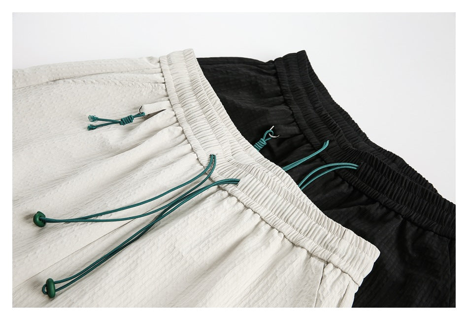 Close view of white and black textured shorts with gathered elastic waists and teal drawcords.