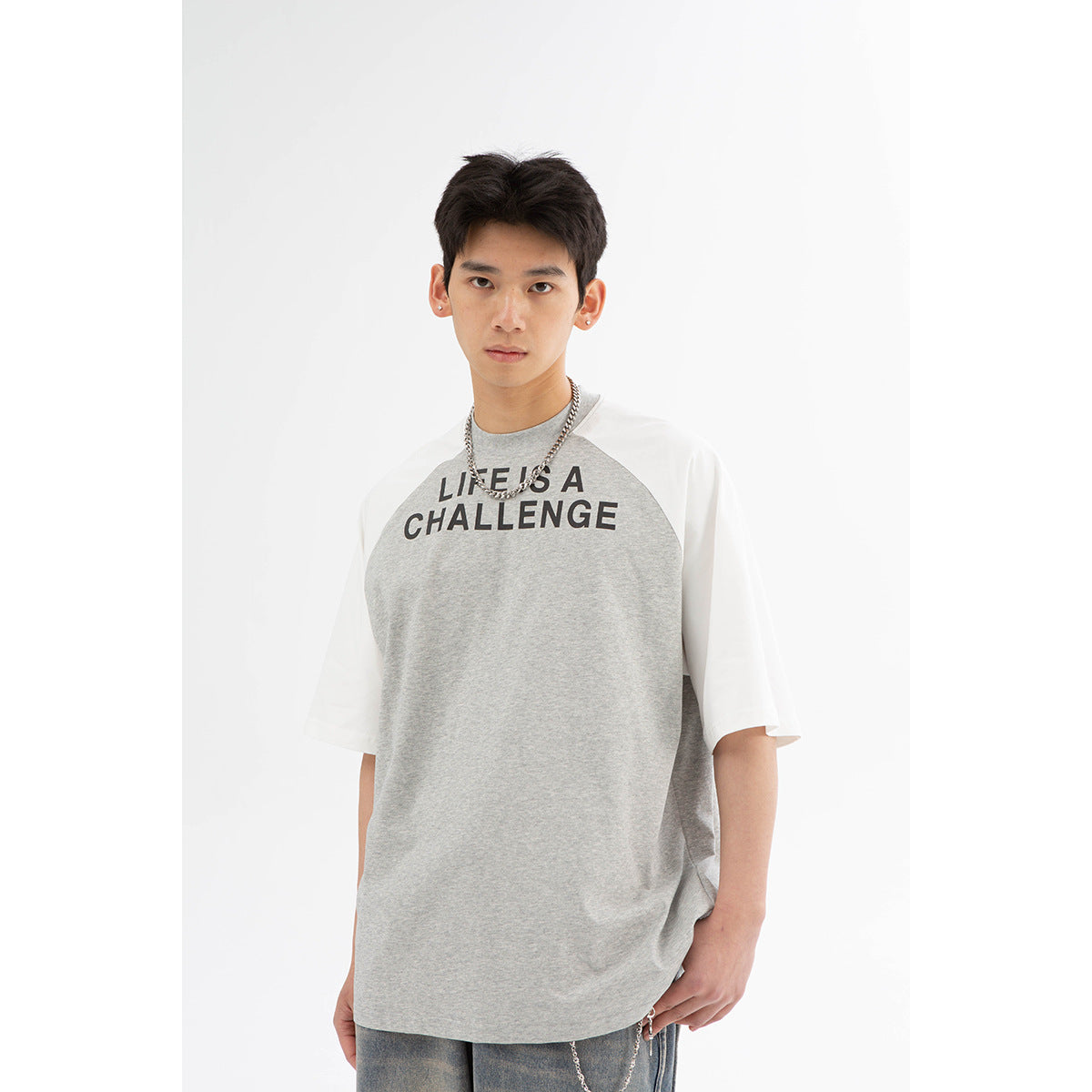 Model wearing a gray raglan T-shirt with white sleeves and black “LIFE IS A CHALLENGE” text.