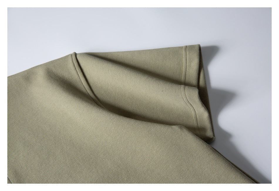 Close-up of a muted olive-beige garment showing a folded edge and neat stitching.