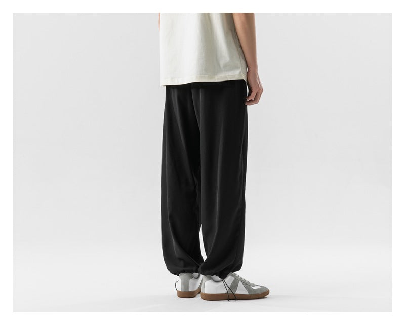 Back view of a model wearing loose black pants with gathered hems and gray sneakers.