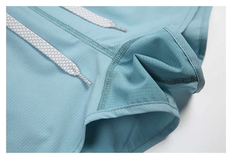 Close-up of blue-green garment seams, gray drawstrings and a curved hem opening.