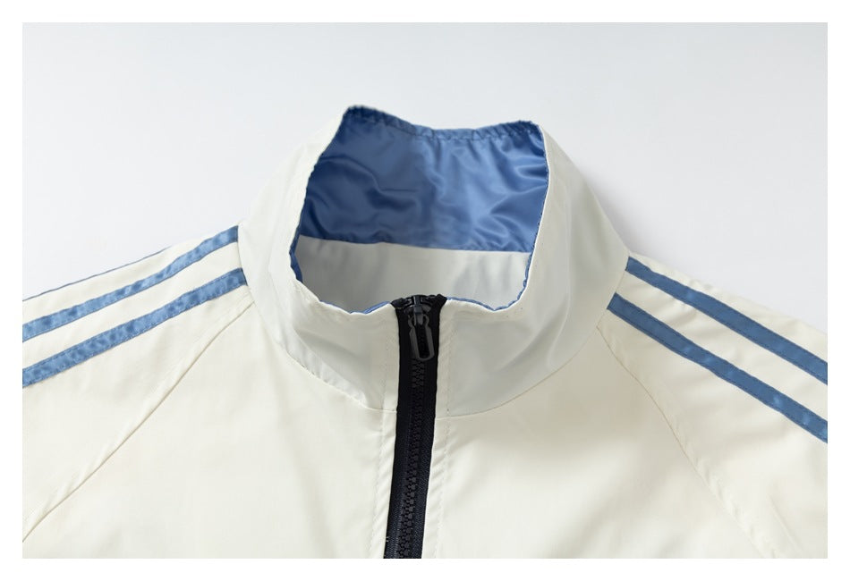 Close-up of a cream jacket's high collar, black front zipper and light blue shoulder stripes.