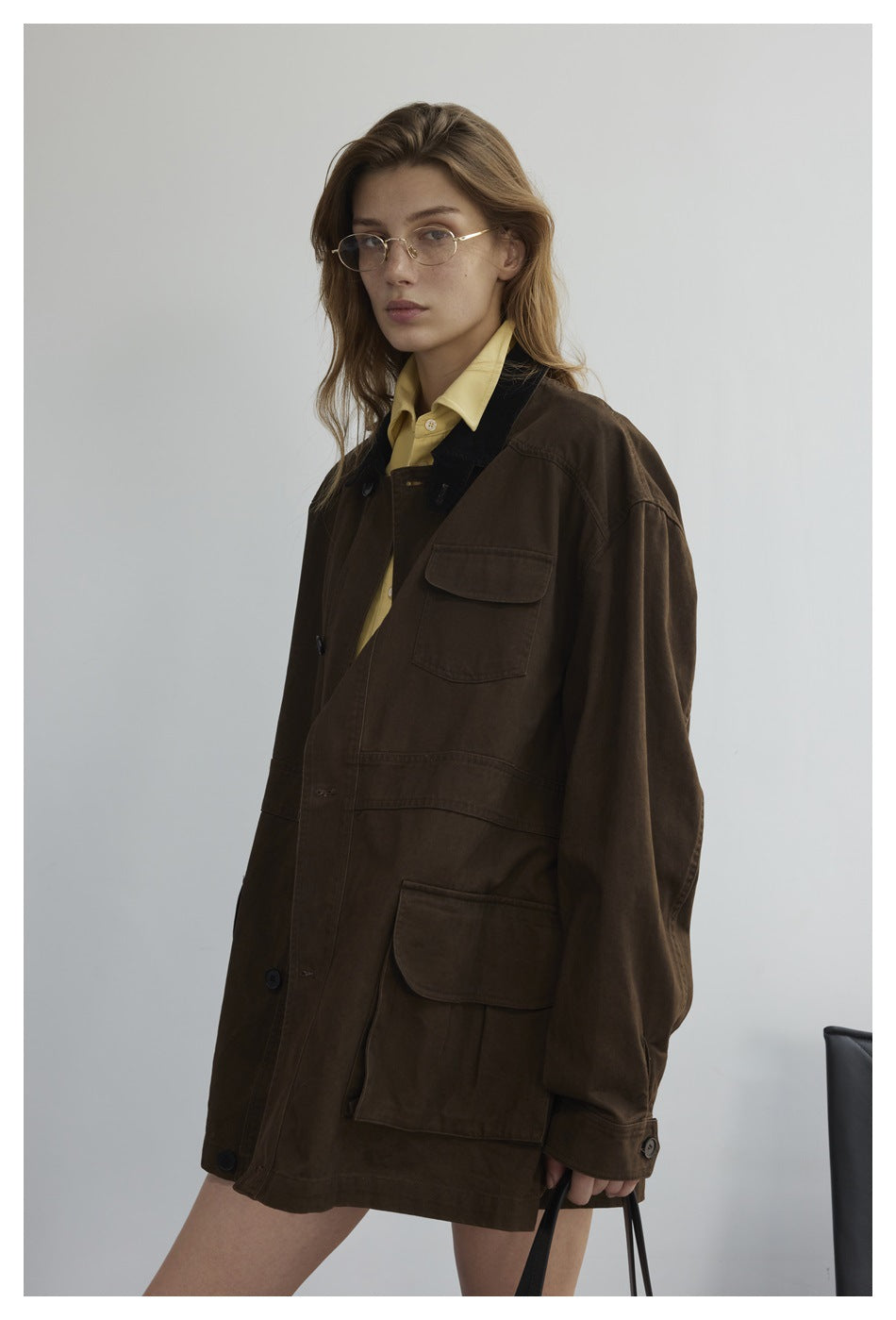 Closer view of a model wearing a dark brown utility jacket with a black collar and large flap pockets.