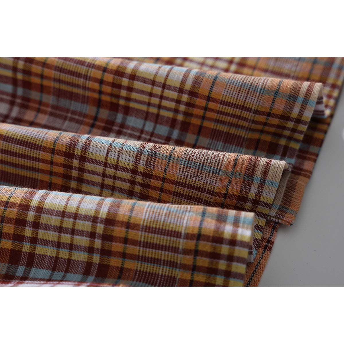 Close-up of folded plaid shirt fabric in rust, tan, cream, blue and yellow tones.