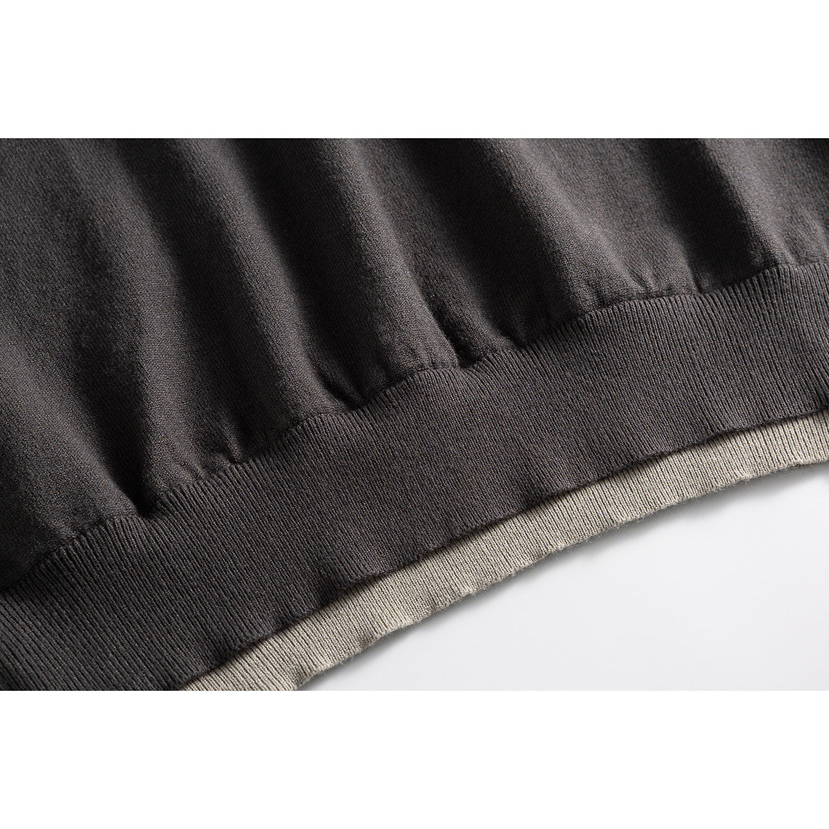 Close-up of a charcoal sweater's gathered hem and ribbed waistband, edged with a beige layer.
