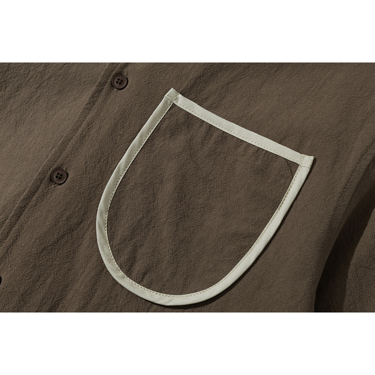 Close-up of a brown shirt's chest pocket with contrasting cream trim and dark buttons.