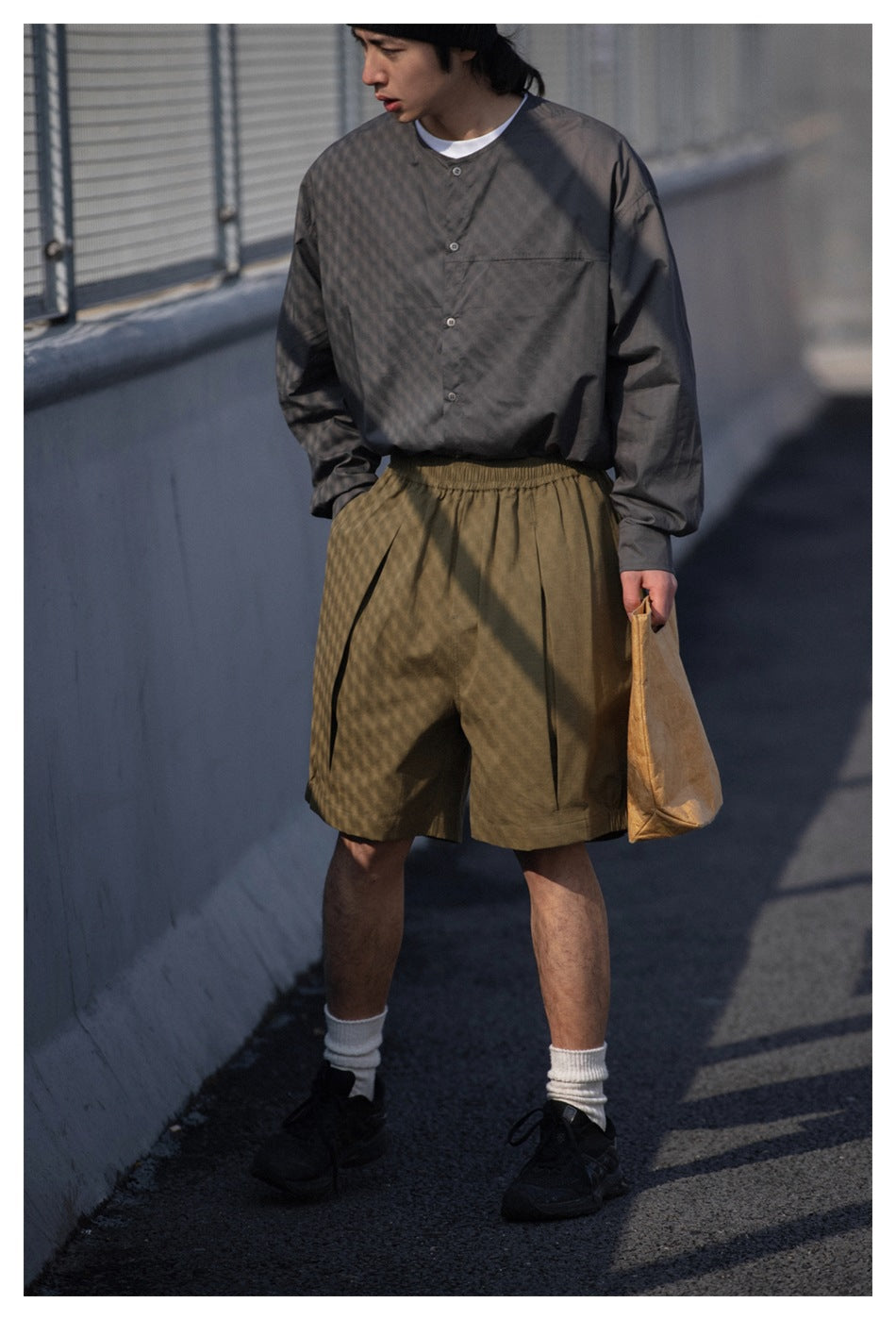 Model wearing loose olive shorts with a gray button-front shirt and chest pocket.